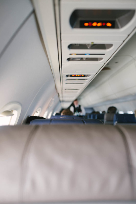 Interior view of an airplane cabin, showing the overhead compartments and seatbelt signs illuminated, with empty and partially occupied seats visible. The image is focused on the cabin ceiling. by Justin Salem Meyer