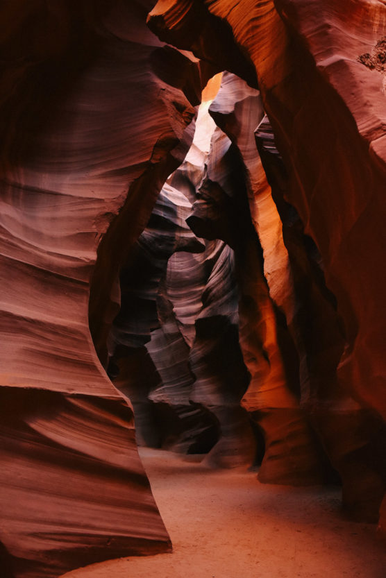 Narrow passage inside a slot canyon with smooth, layered red and orange sandstone walls and sunlight illuminating the curves from above. by Justin Salem Meyer