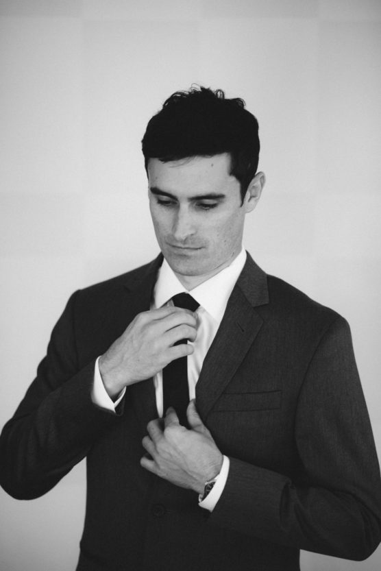 A man in a suit adjusts his tie while looking down. The image is in black and white, creating a classic and formal atmosphere. by Justin Salem Meyer