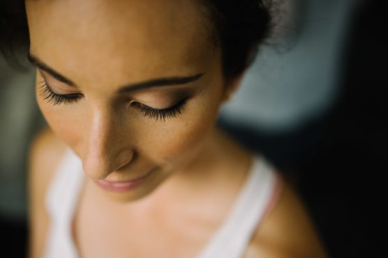 Close-up, top-down view of a woman with closed eyes, long eyelashes, and subtle makeup, wearing a white top. The lighting softly highlights her calm, serene expression. by Justin Salem Meyer