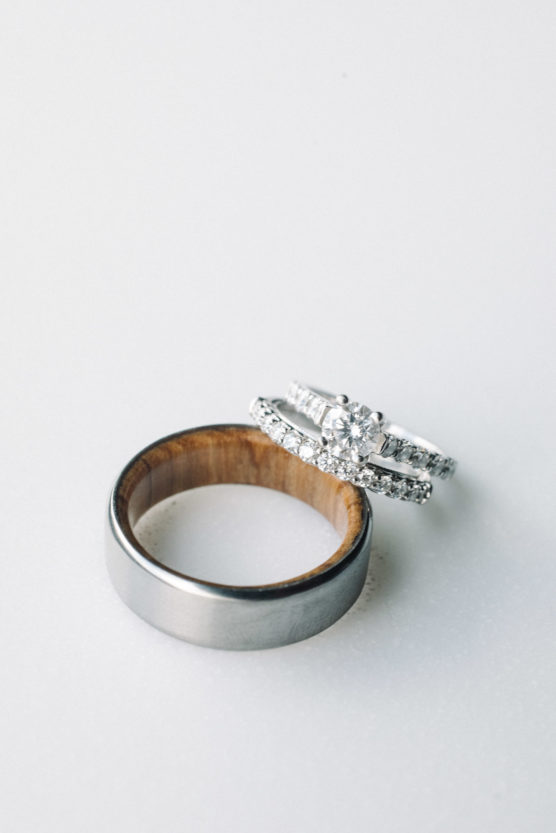 A silver wedding band with a wooden interior is next to an engagement ring and diamond-studded wedding ring set, all displayed on a white surface. by Justin Salem Meyer