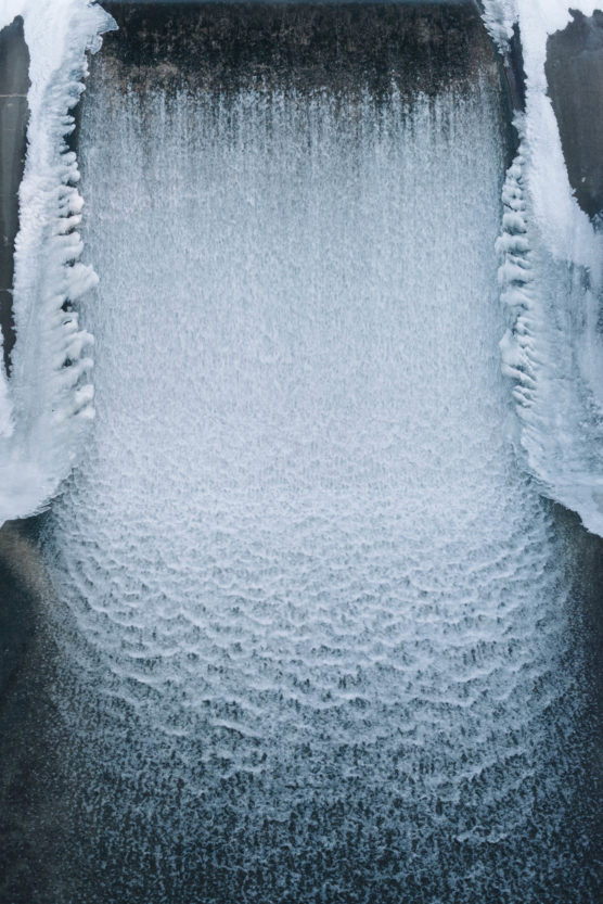 A cascade of water flows down a concrete surface, with patches of snow and ice clinging to the edges, creating a wintry scene. by Justin Salem Meyer