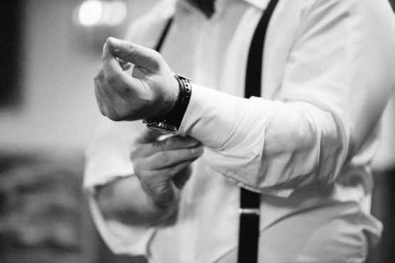 A person in a dress shirt with suspenders is adjusting their shirt cuff. The image is in black and white, and only the torso and arms are visible. by Justin Salem Meyer
