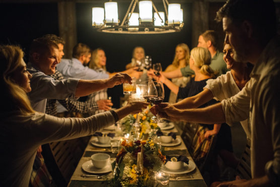 A group of people sit around a decorated dinner table, raising glasses in a toast under a chandelier, sharing a joyful evening together. by Justin Salem Meyer
