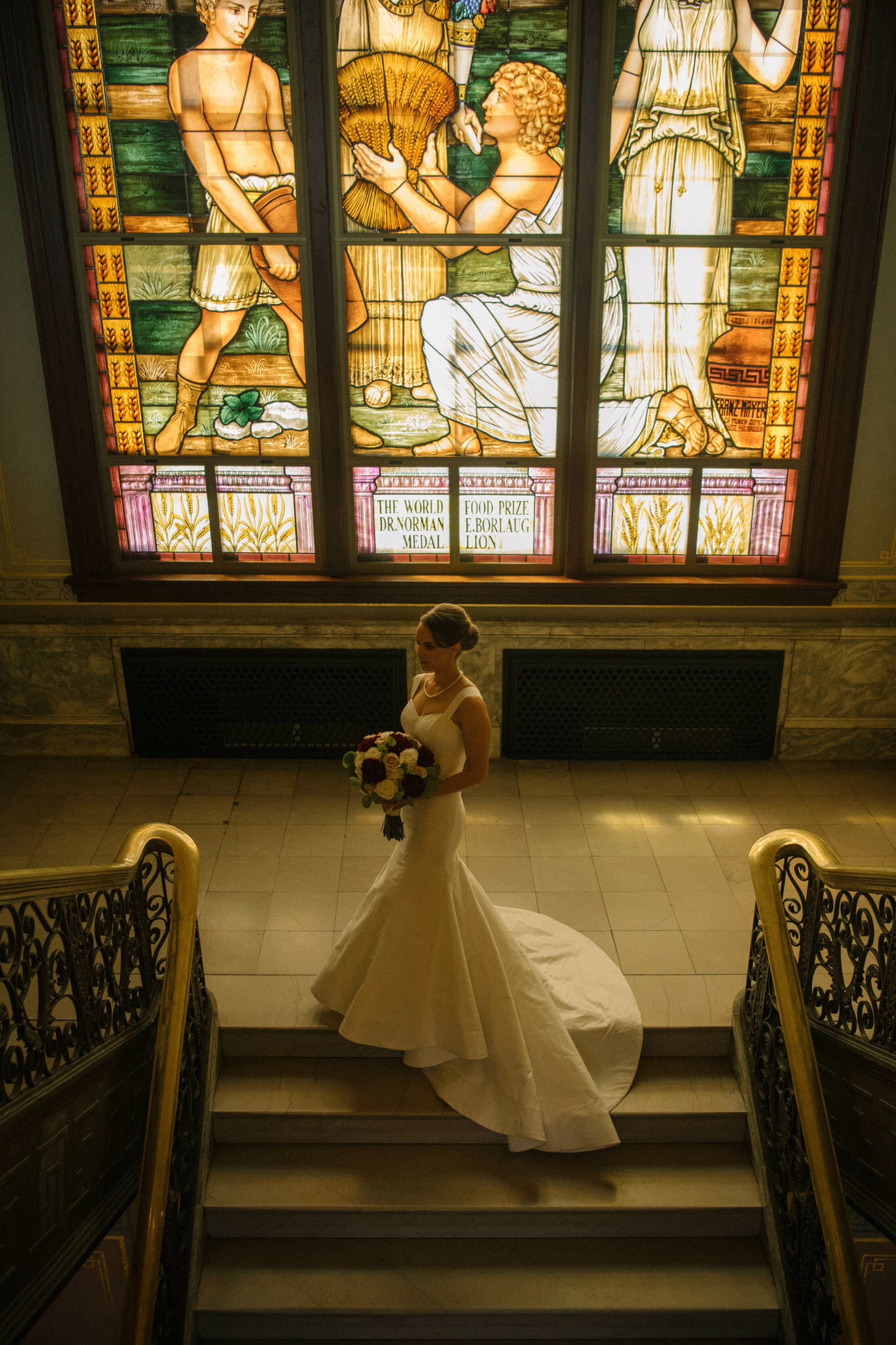 Gorgeous bride standing in the sunlight coming through the large stained glass window at the World Food Prize Hall of Laureates in Downtown Des Moines, Iowa