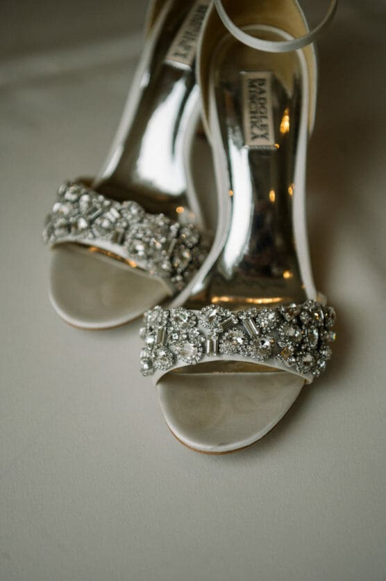 A close-up of elegant high-heeled sandals with sparkling rhinestone embellishments on the front straps, placed on a soft, light-colored surface. by Justin Salem Meyer